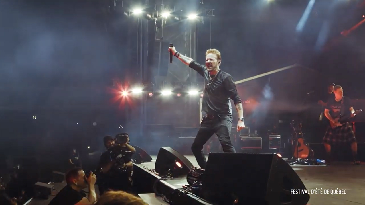 Corey Hart holding his mic above his head on stage